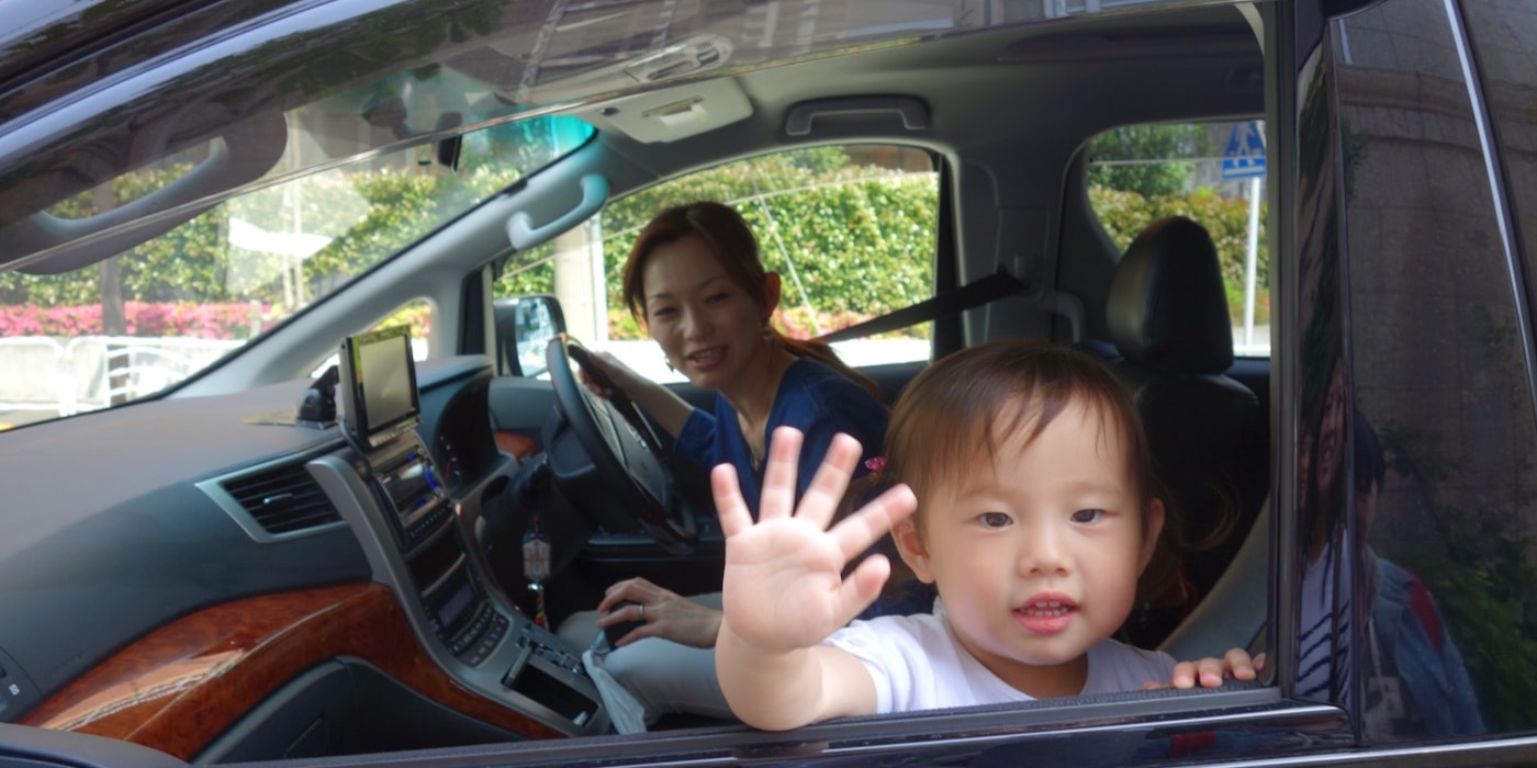 母亲开车、孩子在后座向窗外挥手的家庭用车场景
